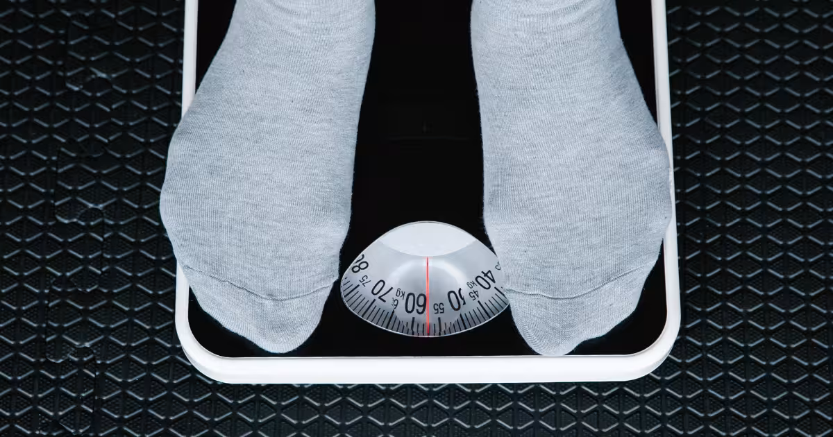 Fitness athlete or person measuring waist with a tape and a scale nearby, representing body mass index calculation