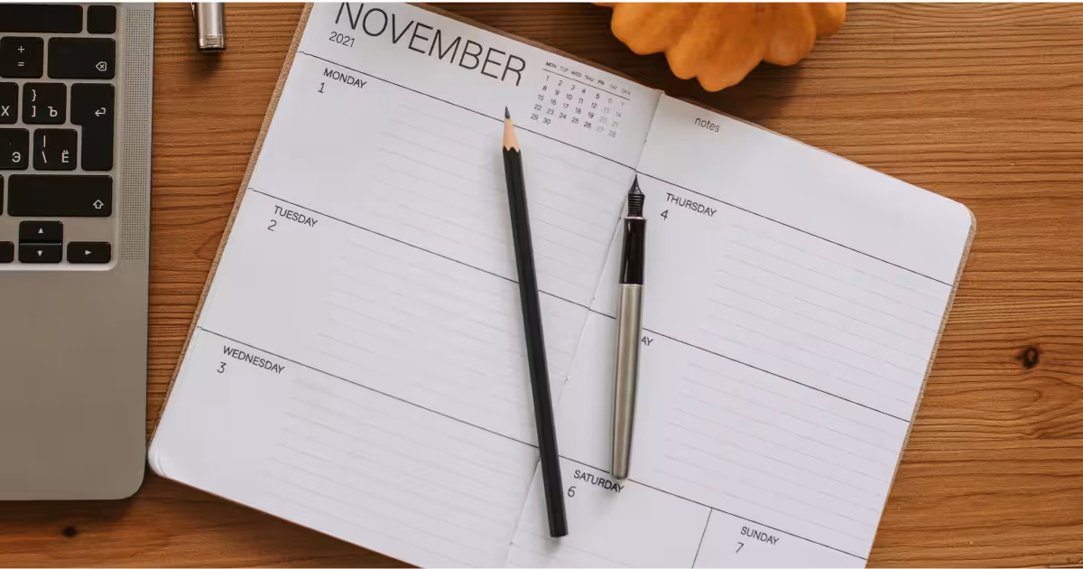 Open calendar on a wooden desk with a pencil and fountain pen for date calculation